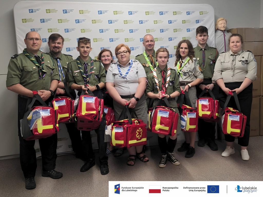 uczestnicy kursu kpp trzymający w rękach apteczki na tle ścianki z logiem zhp